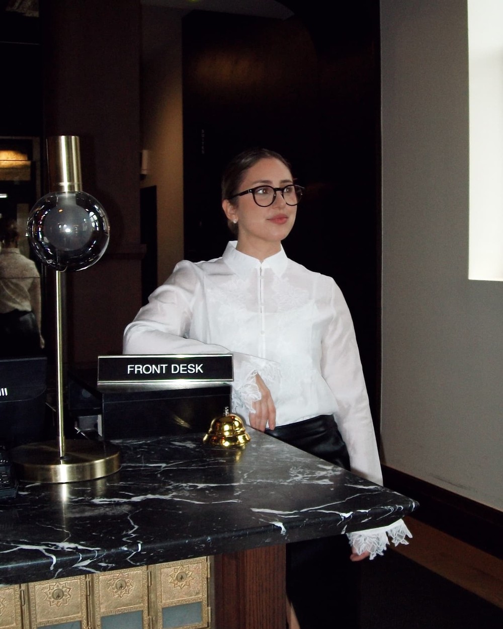 A front desk with a brass lamp and call bell on a dark marble counter